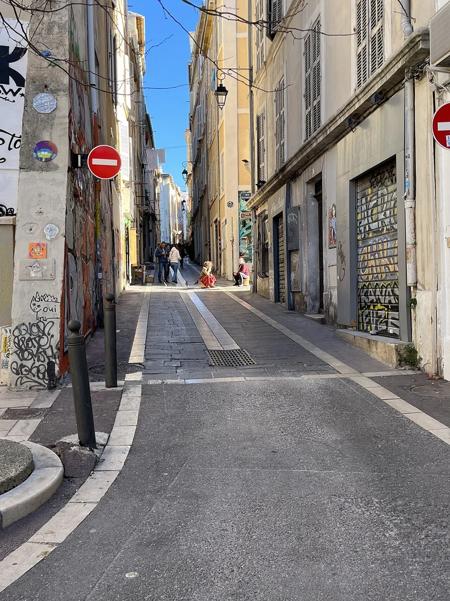 Rue étroite du Panier : façades claires, graffitis et ciel bleu.